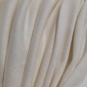 May include: Close-up of a soft, white fabric with a smooth, even texture. The fabric is folded and draped, creating a series of gentle curves and folds.