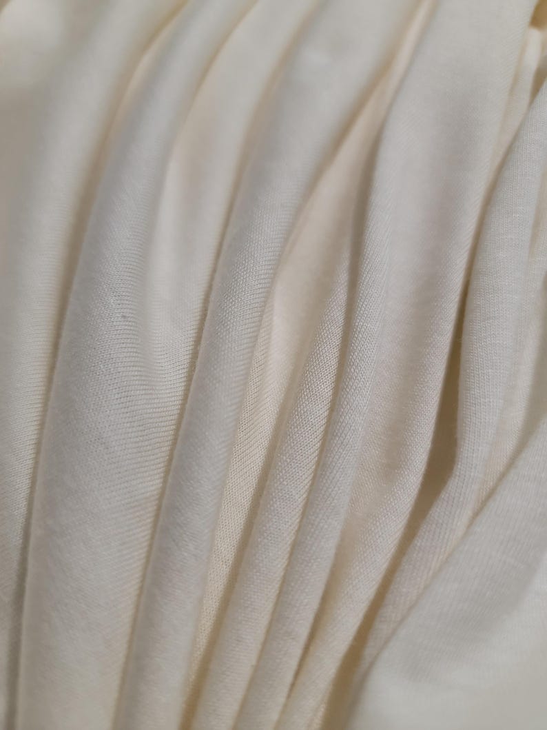 May include: Close-up of a soft, white fabric with a smooth, even texture. The fabric is folded and draped, creating a series of gentle curves and folds.