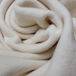 May include: Close-up of a soft, white fabric with a textured surface. The fabric is folded and draped in a way that creates a swirling pattern.