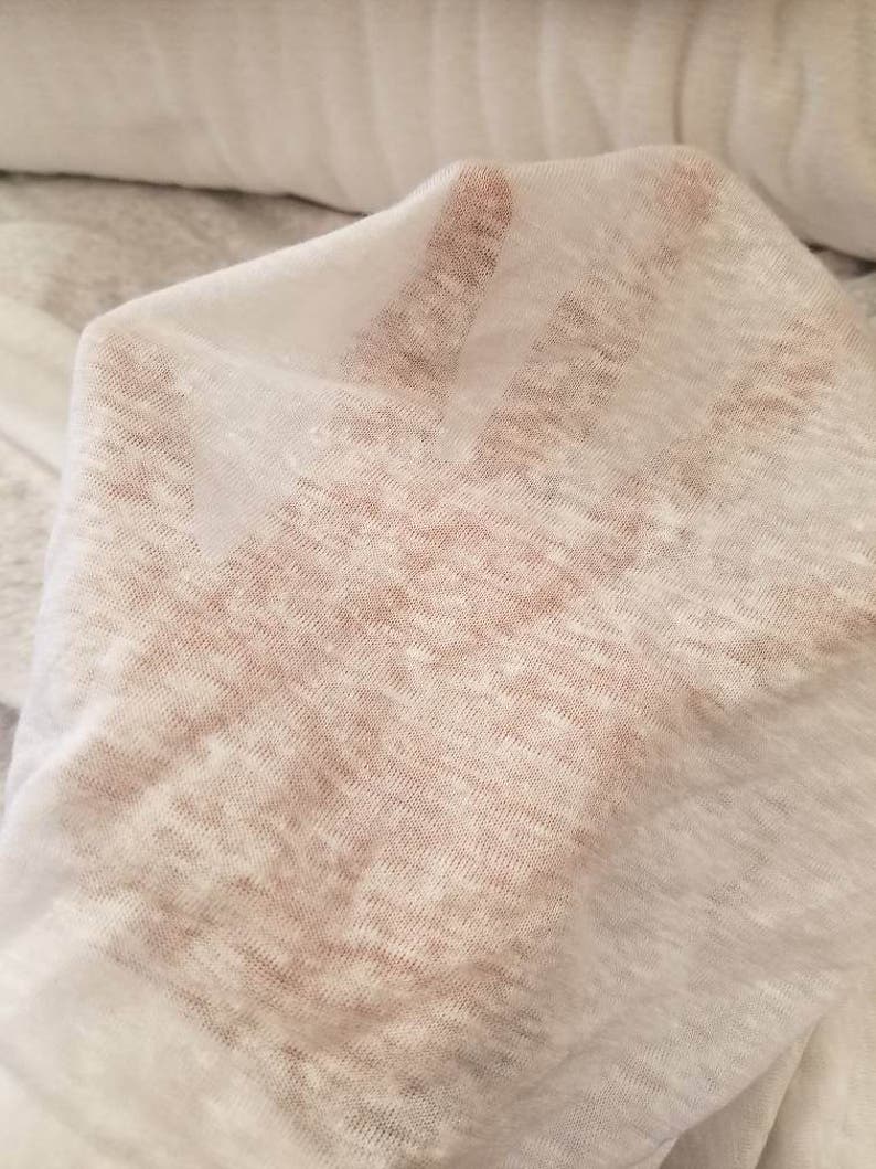 Puede incluir: Tela blanca transparente con una superficie texturizada ligeramente rugosa. La tela es ligera y tiene un brillo sutil.