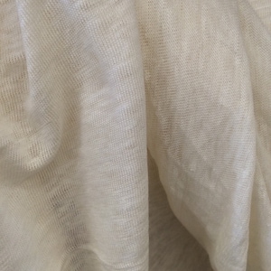 Op de afbeelding: Close-up van een witte stof met een textuurweefsel. De stof is gevouwen en gedrapeerd, waardoor de zachte, natuurlijke textuur zichtbaar is.