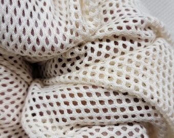 May include: A cream-colored mesh produce bag featuring a repeating diamond-shaped grid pattern. The fabric is lightweight and semi-transparent, showing a soft texture with visible folds and gathers that create depth across the surface of the material.