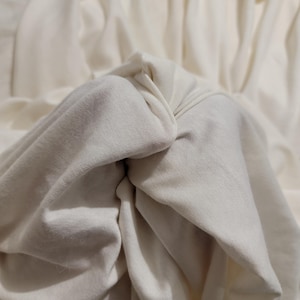 May include: Close-up of a white fabric with soft folds and wrinkles. The fabric is smooth and appears to be made of a natural material.