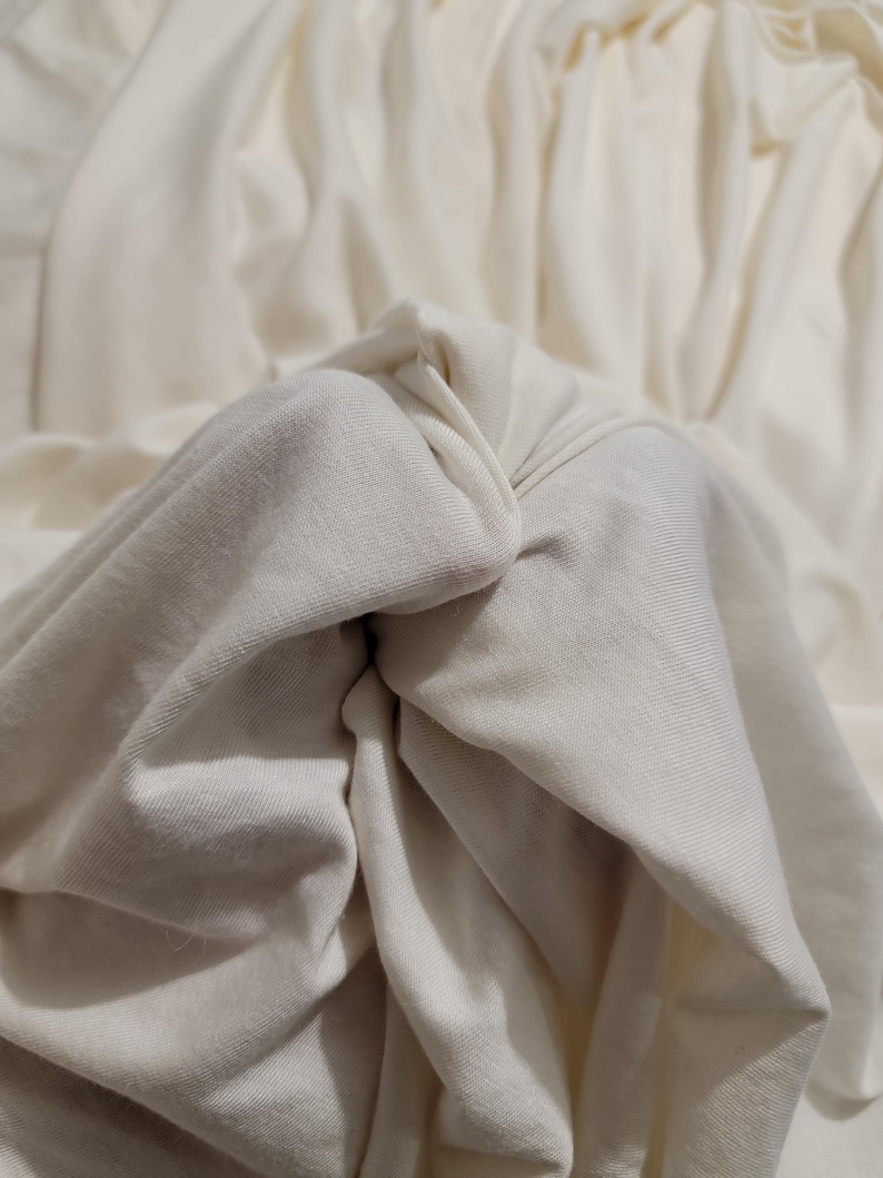 May include: Close-up of a white fabric with soft folds and wrinkles. The fabric is smooth and appears to be made of a natural material.