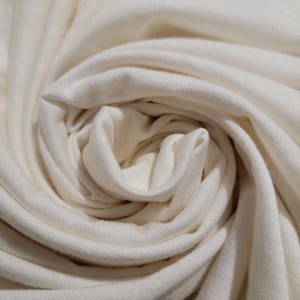 May include: Close-up of a white fabric with a soft, smooth texture. The fabric is folded and twisted, creating a swirling pattern.