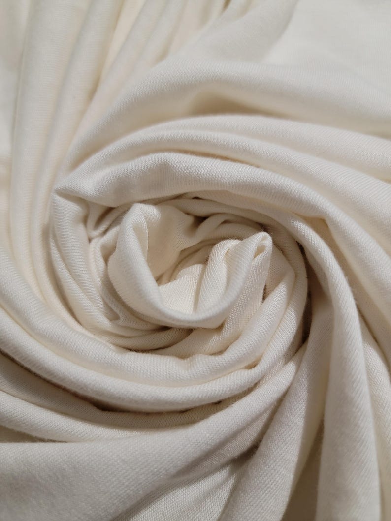 May include: Close-up of a white fabric with a soft, smooth texture. The fabric is folded and twisted, creating a swirling pattern.