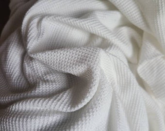 May include: White waffle knit fabric with a textured surface. The fabric is folded and draped, showing the soft and comfortable texture.