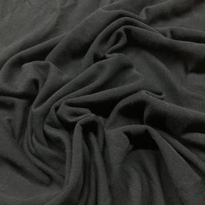 Könnte beinhalten: Nahaufnahme eines schwarzen Stoffes mit sichtbaren Falten und weicher Textur. Das Material scheint drapiert zu sein und erzeugt Schatten und Lichtreflexe. Der Stoff wird wahrscheinlich für Kleidung oder Heimdekoration verwendet.