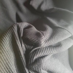 May include: Close-up of black ribbed fabric, showing the texture and folds of the material. The fabric appears to be a knit, possibly for clothing. The image highlights the dark color and the vertical ribbing.