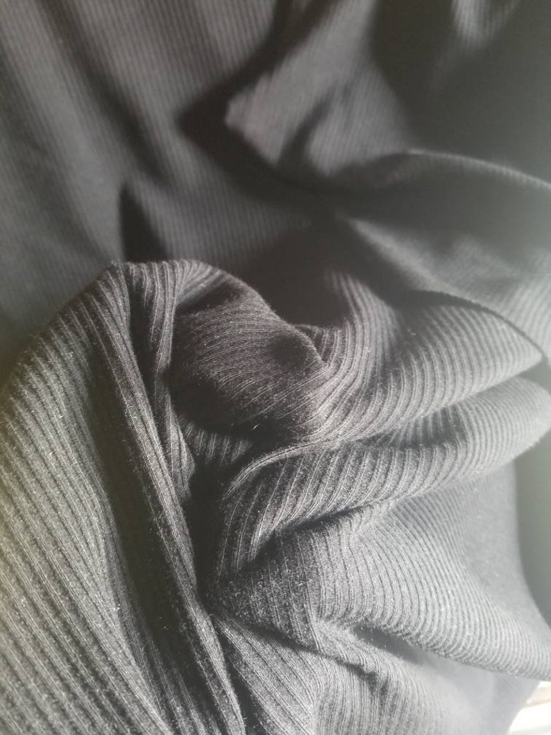 May include: Close-up of black ribbed fabric, showing the texture and folds of the material. The fabric appears to be a knit, possibly for clothing. The image highlights the dark color and the vertical ribbing.