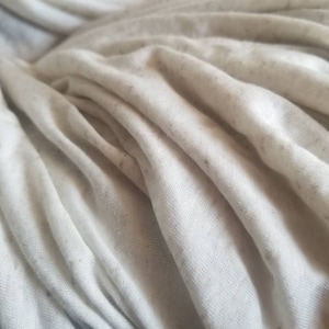 Könnte beinhalten: Nahaufnahme eines weißen Stoffes mit einem dezenten, gesprenkelten Muster. Der Stoff ist zerknittert und gefaltet, wodurch eine strukturierte Oberfläche entsteht.