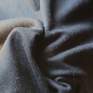 Puede incluir: Primer plano de una tela azul oscuro con una superficie texturizada. La tela está doblada y arrugada, mostrando la textura y la profundidad del material.