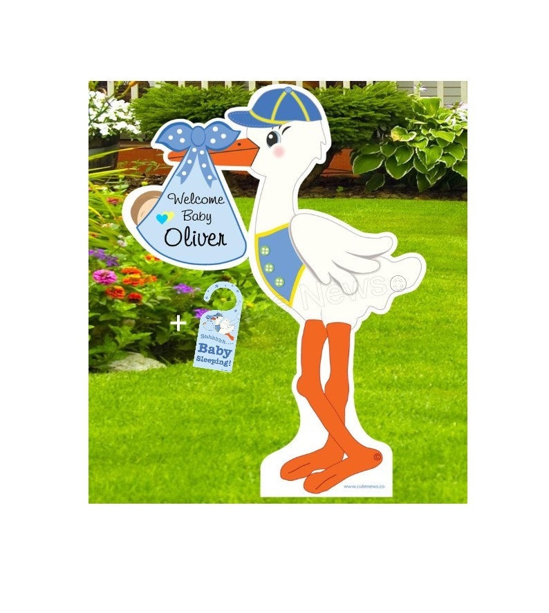Op de afbeelding: Een blauwe en witte ooievaar die een blauwe babybundel vasthoudt met een gele strik en de tekst "Welkom Baby Oliver". Een apart blauw en wit bordje zegt "Sst... Baby slaapt!"