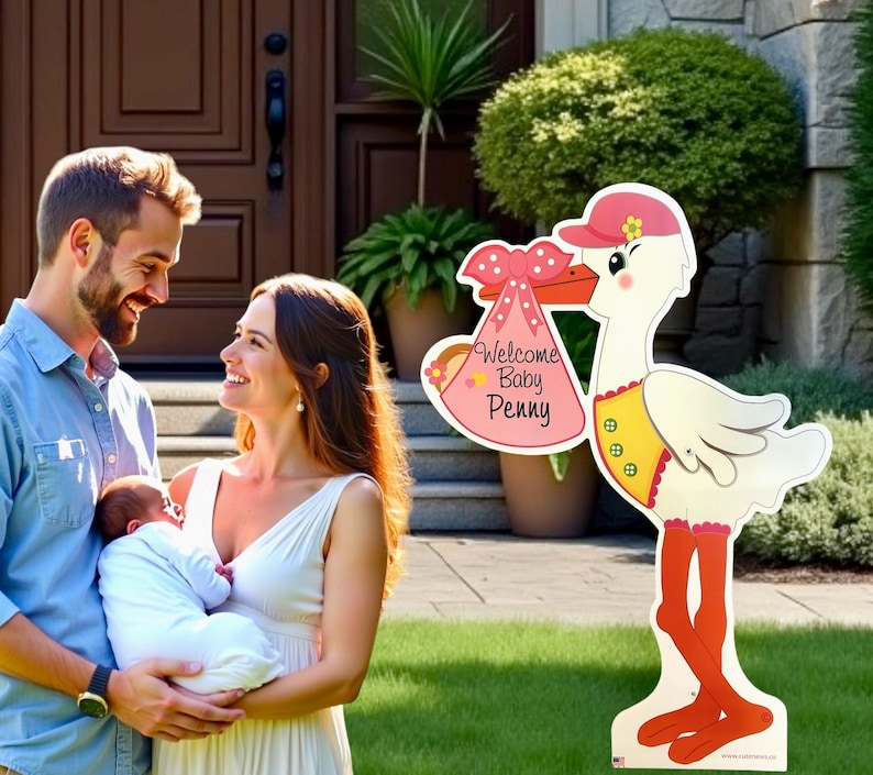 Op de afbeelding: Een roze en witte ooievaar die een roze en witte babytas vasthoudt met de tekst "Welcome Baby Penny". De ooievaar staat op een groen gazon voor een huis.