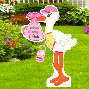 May include: Pink and white stork holding a pink and white baby announcement sign that says "Welcome Baby Olivia". A separate pink and white sign says "Shhh... Baby Sleeping!"