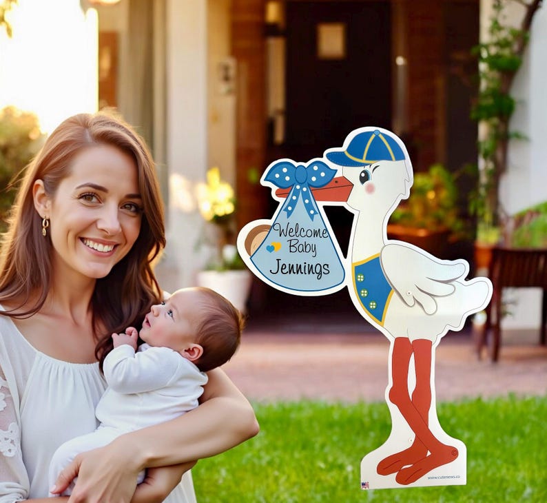 Op de afbeelding: Een witte ooievaar met een blauwe hoed en een blauwe en witte luiertas met de tekst "Welkom Baby Jennings". De ooievaar houdt de tas in zijn bek. De ooievaar staat op een groen gazon.