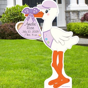 May include: A white stork with a purple hat and bow holds a purple and white baby bag with the text "Amelie Rose, July 10, 2025, 7 lbs. 5 oz."  The stork is standing on a green lawn.