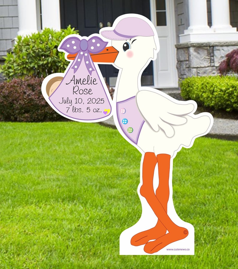 May include: A white stork with a purple hat and bow holds a purple and white baby bag with the text "Amelie Rose, July 10, 2025, 7 lbs. 5 oz."  The stork is standing on a green lawn.