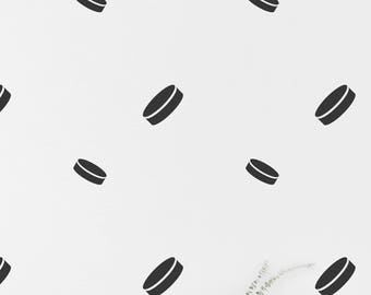 May include: A white wall with black hockey puck decals. A white desk with a chair sits in front of the wall. The desk has a framed picture and a small plant on it.