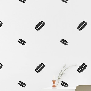 May include: A white wall with black hockey puck decals. A white desk with a chair sits in front of the wall. The desk has a framed picture and a small plant on it.