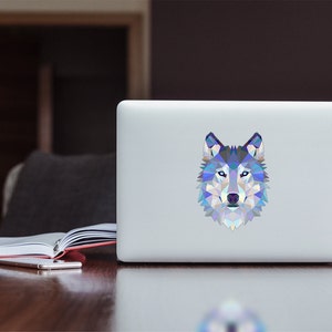 May include: A white laptop with a geometric wolf sticker on the lid. The wolf is blue, purple, and white.