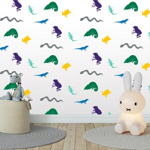 May include: A white wall with a repeating pattern of green, blue, and purple frogs, lizards, and snakes. There are also yellow fish shapes. A gray stuffed animal and a white rabbit nightlight are in the foreground.