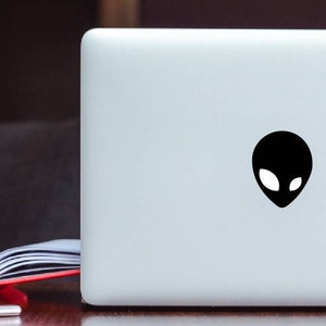 Puede incluir: Un ordenador portátil blanco con una pegatina de cabeza de extraterrestre negra en la tapa.