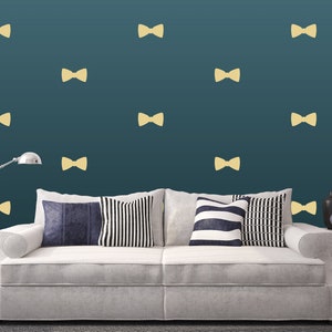 May include: A white couch with pillows in a living room with a teal wall. The wall is decorated with gold bow tie stickers.