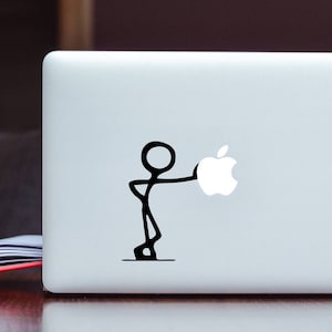 Op de afbeelding: Een witte laptop met een zwart stick figure dat een witte Apple-logo sticker vasthoudt.