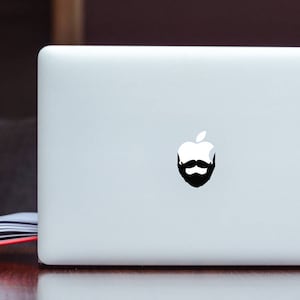 May include: A silver laptop computer with a black and white sticker of an apple with a beard on the lid.