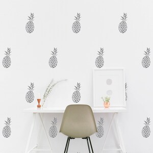 Puede incluir: Una pared blanca con un escritorio y una silla delante. La pared está decorada con un patrón repetitivo de siluetas de piña grises.