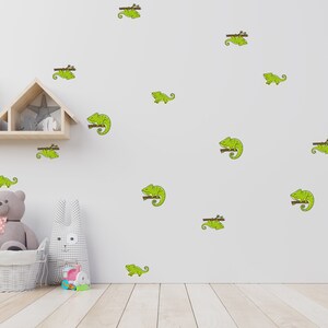 May include: A white wall with a variety of green chameleon wall decals. The decals feature the chameleon sitting on a branch. There is a wooden shelf with a stuffed animal and a toy on it.