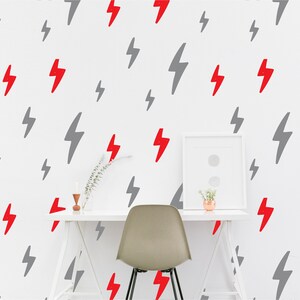 Puede incluir: Una pared blanca con un patrón repetido de rayos grises y rojos. Un escritorio blanco con una silla gris se encuentra frente a la pared. Una pequeña planta en maceta se encuentra sobre el escritorio.