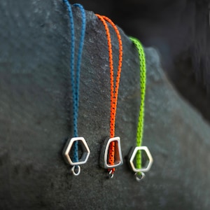 Peut inclure: Trois porte-clés argentés avec des formes géométriques sont suspendus à des cordons de différentes couleurs : sarcelle, orange et vert citron.