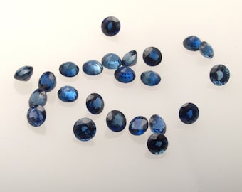 May include: A collection of loose, round, blue gemstones. The gemstones are scattered on a white surface.