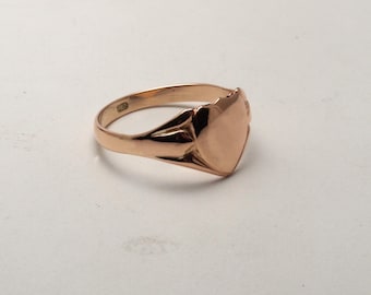 May include: A gold signet ring with a heart-shaped top. The ring is smooth and polished.