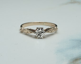 May include: A gold ring featuring a single diamond set in a starburst design. The ring has a delicate, intricate design with a polished finish.