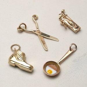 May include: Four gold-colored charm pendants: a pair of scissors, a boot, a frying pan with a fried egg, and a golf bag.