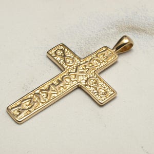 Puede incluir: Un colgante de cruz de oro con detalles intrincados y una superficie texturizada. La cruz es un símbolo religioso y a menudo se usa como collar.