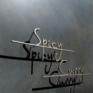 May include: A close-up of a dark grey wall featuring the words "Spicy Curry" in a metallic, cursive font. The words are connected by horizontal lines, creating shadows. The image evokes a restaurant or food-related setting.