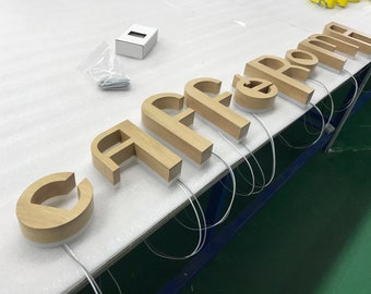May include: Wooden letters spelling out "Caffe Roma" on a white surface. The letters are illuminated from within and have a warm, natural wood finish.