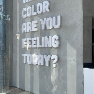 K&ouml;nnte beinhalten: Eine wei&szlig;e Wand mit dem Text "Welche Farbe f&uuml;hlst du dich heute?" in gro&szlig;en, wei&szlig;en 3D-Buchstaben.