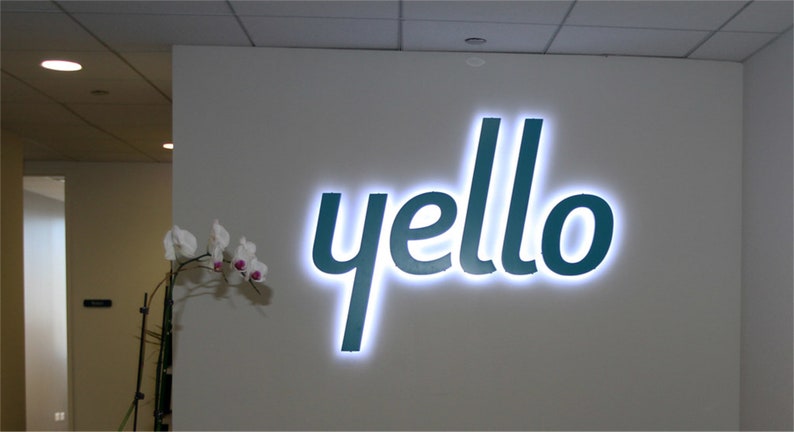 以下が含まれることがあります： 白い壁に、白く縁取られたターコイズブルーの「yello」の看板が取り付けられています。