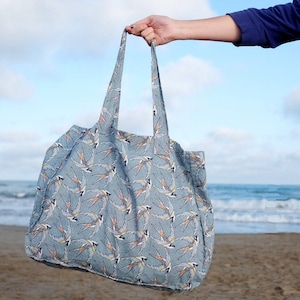 May include: A large blue tote bag with a white and yellow bird pattern. The bag has two handles and is made of a soft, fabric material.