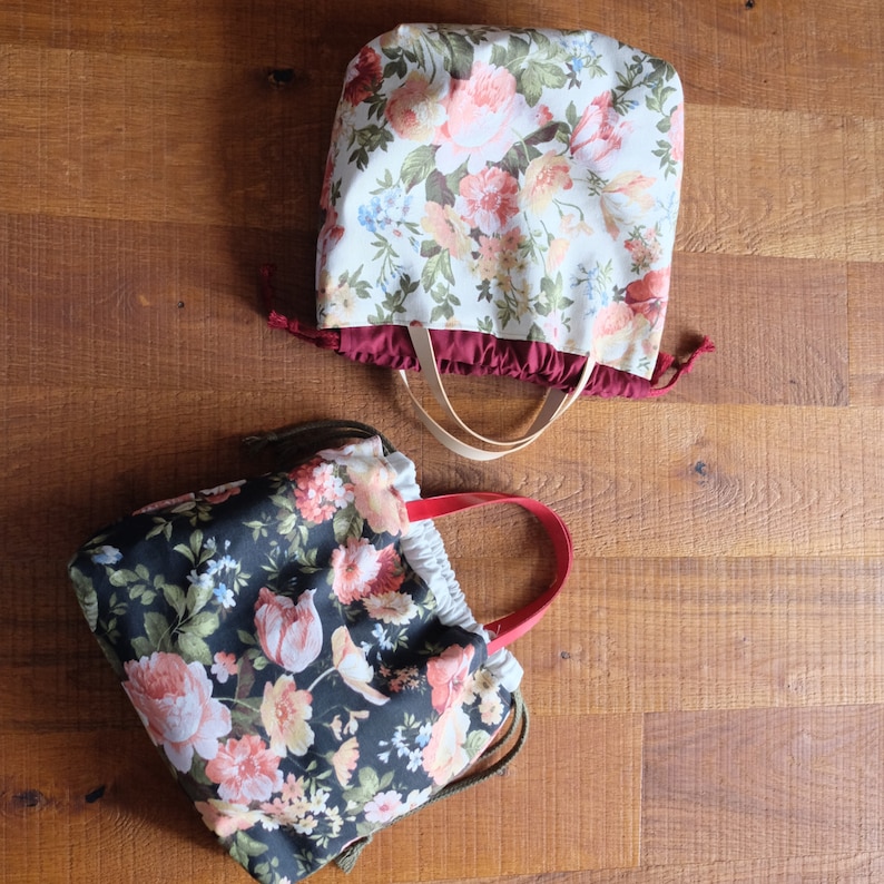 May include: Two floral print fabric bags with handles. One bag is red with white flowers and the other is black with white and pink flowers.