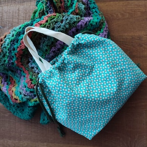 May include: A teal blue drawstring bag with a white and orange geometric pattern. The bag is made of fabric and has a white drawstring.