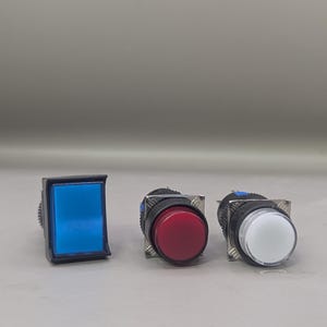 May include: Three electrical push buttons with different coloured button faces. One is square and blue, the others are round, one red and one white. All have black and silver housings.