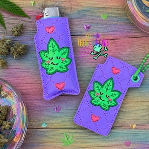 May include: Two purple quilted lighter sleeves featuring an embroidered green leaf character with a smiling face and pink cheeks, accented by small pink hearts. One sleeve is fitted over a lighter, while the other has a green ball chain attached.