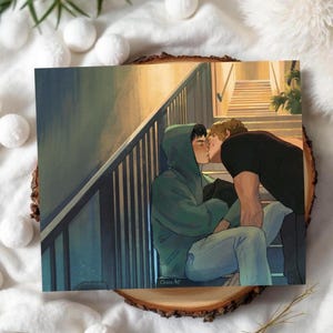 以下が含まれることがあります： 階段でキスをしている2人を描いたアートプリント。一人は緑色のパーカー、もう一人は黒いシャツを着ています。このアートワークは、人物と建築的な細部に焦点を当てた、暖色系の色使いをしています。