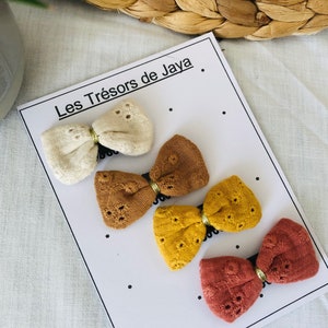May include: Four fabric hair bows in different colors: cream, brown, yellow, and red. The bows are displayed on a white card with the text "Les Tr&eacute;sors de Jaya".